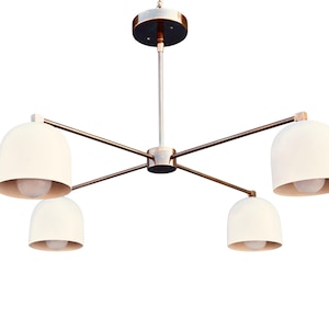 Peut inclure: Un lustre moderne avec cinq abat-jours en forme de cloche de couleur blanc cassé. Le luminaire a une finition bronze avec une tige centrale et des bras s'étendant vers l'extérieur. Chaque abat-jour abrite une ampoule, créant une lueur chaleureuse et accueillante.