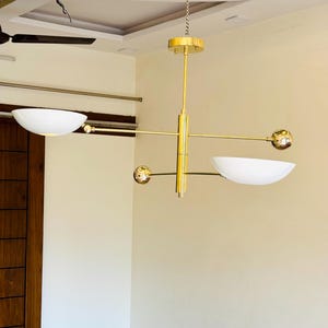 May include: A gold modern chandelier with three white bowl-shaped light fixtures and gold spheres. The chandelier is hanging from a chain.