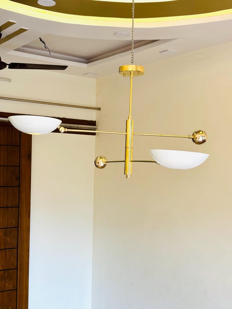 May include: A gold modern chandelier with three white bowl-shaped light fixtures and gold spheres. The chandelier is hanging from a chain.