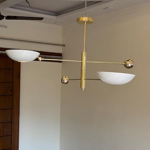 May include: A gold-toned modern chandelier with three white bowl-shaped shades and gold spheres. The chandelier is suspended from the ceiling by a chain.