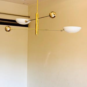 May include: A gold-toned modern chandelier with four white bowl-shaped light shades and four gold spheres. The chandelier is suspended from the ceiling by a chain.