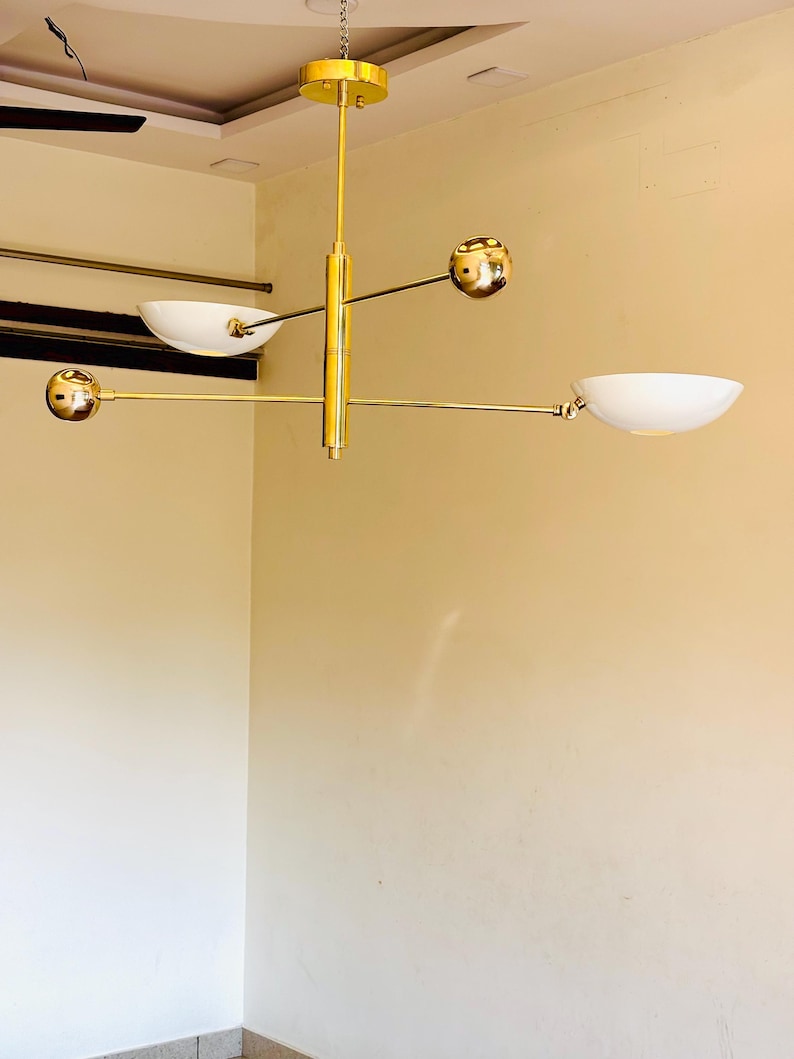 May include: A gold-toned modern chandelier with four white bowl-shaped light shades and four gold spheres. The chandelier is suspended from the ceiling by a chain.