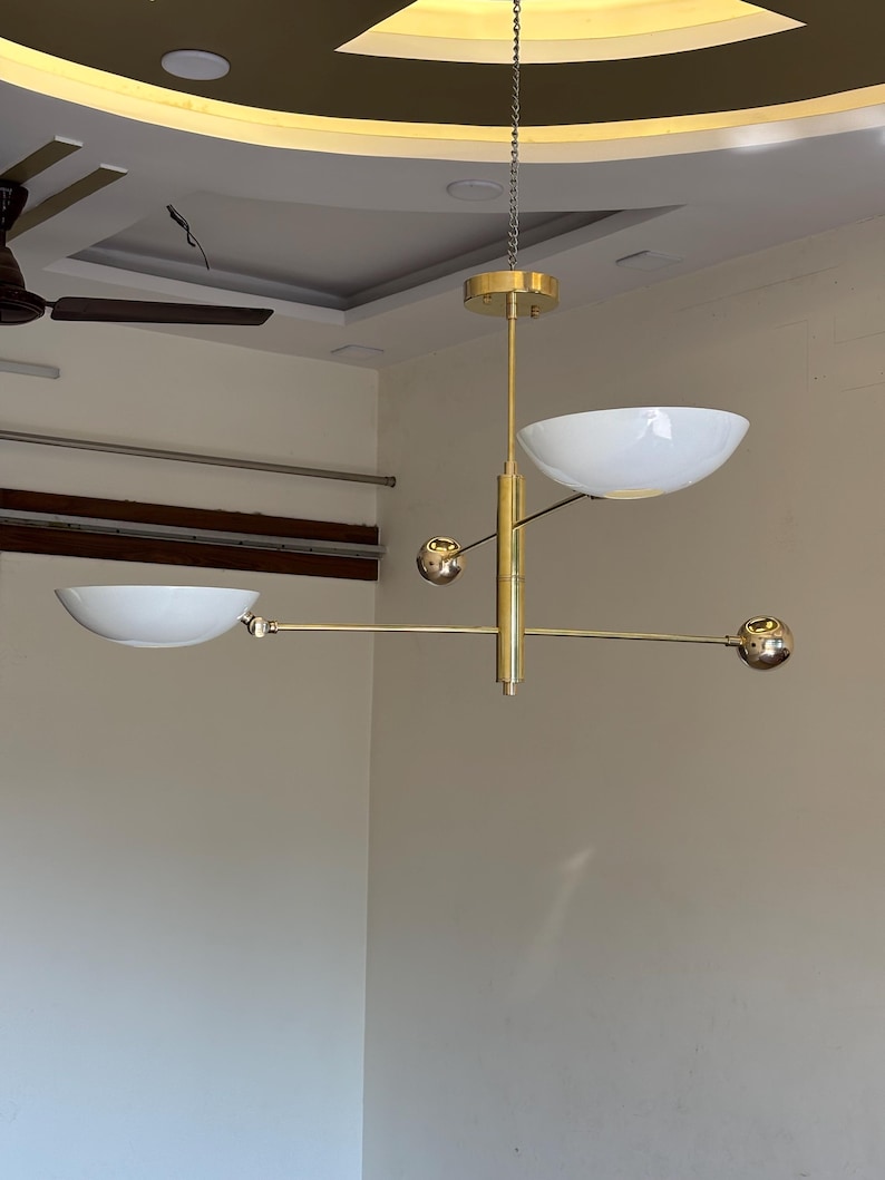 May include: A gold-toned modern chandelier with three white bowl-shaped shades and three gold spheres. The chandelier is suspended from the ceiling by a chain.