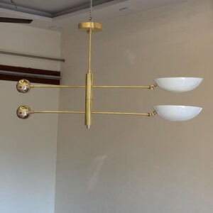 May include: A gold-toned modern chandelier with three round light fixtures and two white bowl-shaped shades.