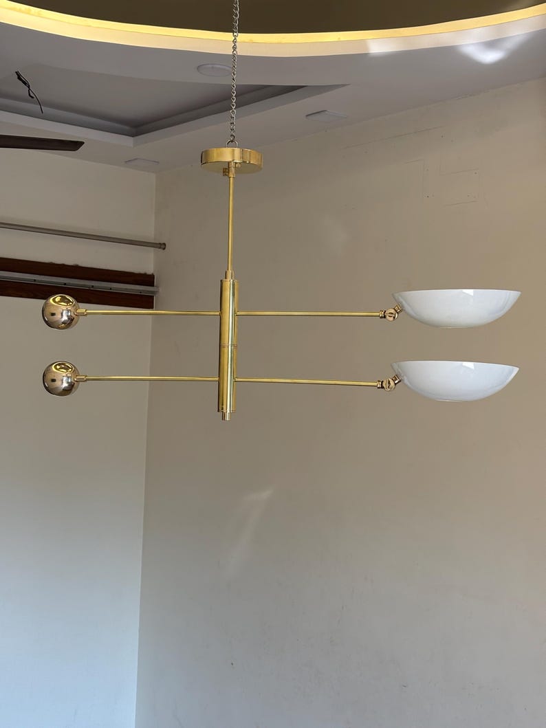May include: A gold-toned modern chandelier with three round light fixtures and two white bowl-shaped shades.