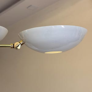 May include: A white, round, ceiling light fixture with a gold metal arm. The light fixture has a simple, modern design.