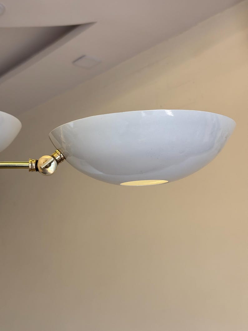 May include: A white, round, ceiling light fixture with a gold metal arm. The light fixture has a simple, modern design.