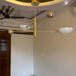 May include: A gold-toned, multi-arm chandelier with white bowl-shaped shades hangs from the ceiling. The chandelier has a modern design with a sleek, minimalist aesthetic.