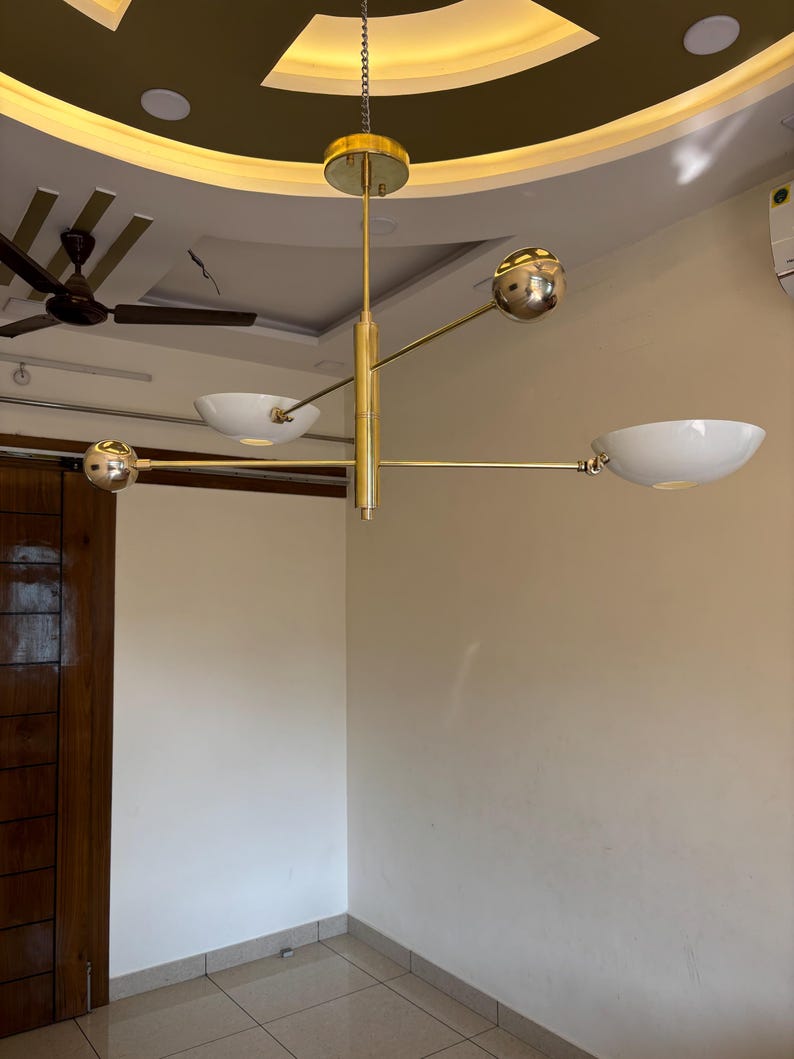 May include: A gold-toned, multi-arm chandelier with white bowl-shaped shades hangs from the ceiling. The chandelier has a modern design with a sleek, minimalist aesthetic.