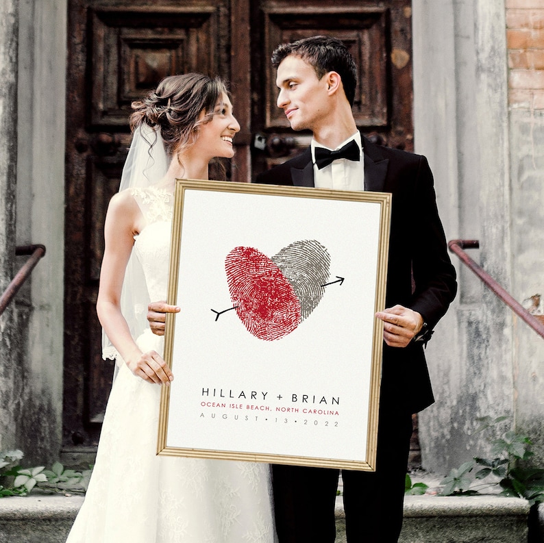 Wedding couple standing in front of church holding fingerprint heart artwork personalized with wedding details.