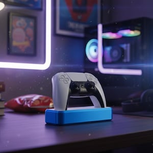 May include: A white and black game controller on a blue stand, with a gaming PC in the background. The desk also has headphones, a snack bag, and books. The room is lit with purple and white lights.