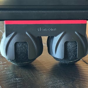 May include: Black furniture mover with a red accent and two felt-bottomed wheels. The text "s1on.com" is printed on the black plastic. The wheels are designed to protect floors while moving furniture.