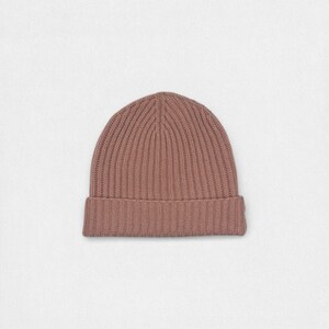 Könnte beinhalten: Eine einfarbige, mauvefarbene Beanie-Mütze. Die Mütze ist aus einem gerippten Strickstoff gefertigt und hat einen umgeschlagenen Saum. Die Beanie ist ein schlichtes, klassisches Design, geeignet für kaltes Wetter. Die Mütze wird vor einem weißen Hintergrund gezeigt.