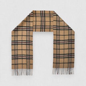 Könnte beinhalten: Beigefarbener Schal mit klassischem Karomuster in Schwarz, Rot und Weiß. Der Schal hat einen Fransenrand und wird flach präsentiert. Dieses Accessoire ist für kaltes Wetter geeignet und verleiht einen Hauch von Stil.