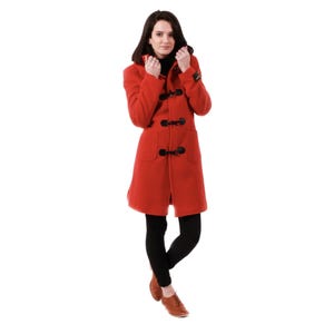 Könnte beinhalten: Ein roter Dufflecoat mit schwarzen Knebelverschlüssen und Kapuze. Der Mantel hat zwei Vordertaschen und wird mit schwarzen Leggings und braunen Schuhen getragen. Ein klassischer Wintermantel.