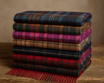 May include: A stack of eight folded plaid blankets in various colors, including teal, pink, brown, and red. The blankets are arranged on a wooden surface, with the bottom blanket having a red fringe.
