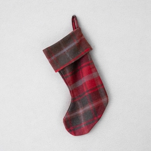 May include: A festive Christmas stocking in a red and grey plaid design. The stocking has a folded cuff and a loop for hanging. The plaid pattern combines red, grey, and brown tones, perfect for the holiday season.