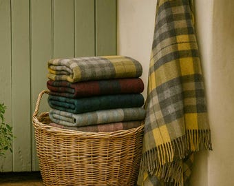 May include: A woven wicker basket filled with a stack of five folded wool blankets in various plaid patterns, including yellow, gray, red, and teal. An additional yellow and gray plaid blanket with fringed edges hangs over the side.