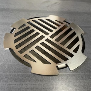 Könnte beinhalten: Ein runder, silberfarbener Abflussdeckel aus Metall mit einem Gittermuster. Der Deckel hat einen leicht erhöhten Rand und ist so konzipiert, dass er auf eine kreisförmige Abflussöffnung passt.