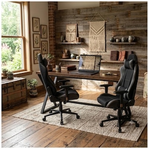 May include: Two black ergonomic gaming chairs with high backrests, adjustable armrests, and five-wheel bases positioned in front of a long wooden desk. Each chair features a headrest pillow and contoured padding for support during extended use.