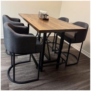 May include: A modern dining set featuring a rectangular wooden table with a dark finish, supported by black metal legs. Four gray upholstered bar stools with curved black metal bases surround the table. A small wire rack and condiments sit on the table.