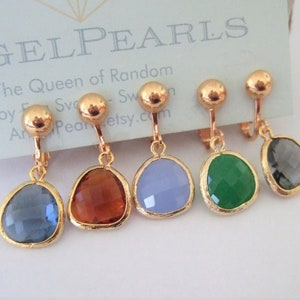 Puede incluir: Cinco pares de pendientes de clip dorados con piedras de cristal de diferentes colores. Las piedras son en tonos de azul, marr&oacute;n, morado, verde y gris.
