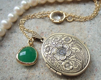 Puede incluir: Un collar con un medallón dorado con diseño floral ovalado, un colgante de piedra verde y un collar de perlas. El medallón está abierto, revelando espacio para una foto o recuerdo.