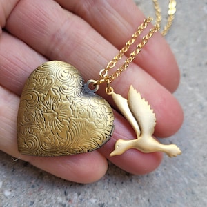 Puede incluir: Collar de oro con un dije en forma de corazón y un dije de pájaro. El dije tiene un diseño floral adornado.