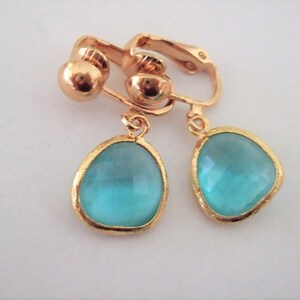 Puede incluir: Un par de pendientes de clip de tono dorado con piedras de vidrio azul turquesa en forma de l&aacute;grima.