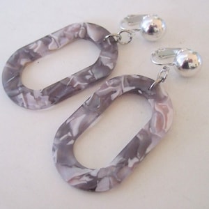 May include: A pair of silver clip-on earrings with oval-shaped gray and white marbled plastic accents.