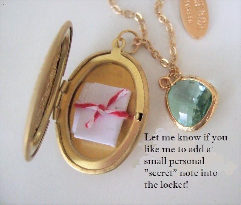 May include: Gold locket necklace with a small white note inside and a green gemstone pendant. The locket is open and the note is visible. The text on the image reads: "Let me know if you like me to add a small personal "secret" note into the locket!"