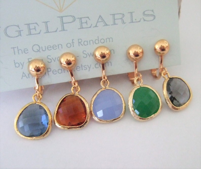 Puede incluir: Cinco pares de pendientes de clip dorados con piedras de cristal de diferentes colores. Las piedras son en tonos de azul, marr&oacute;n, morado, verde y gris.