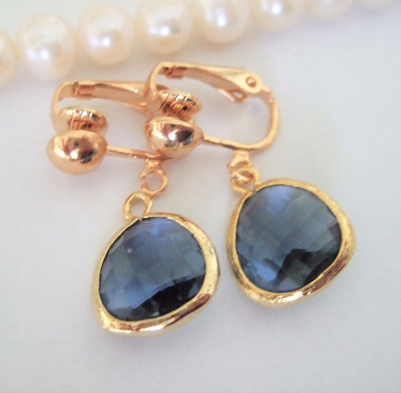 Puede incluir: Un par de pendientes de clip de tono dorado con piedras azules facetadas colgantes.
