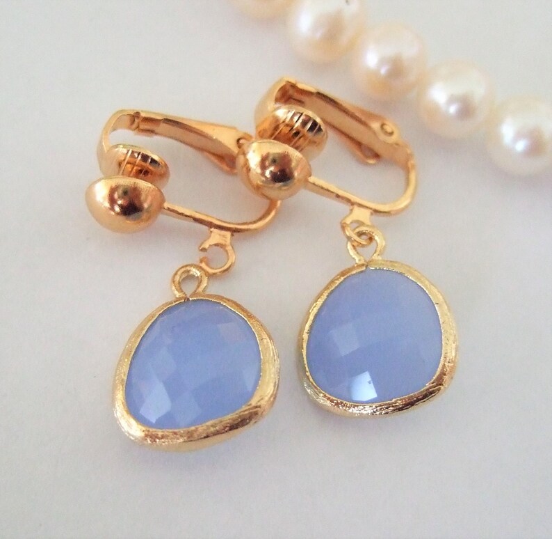 Puede incluir: Un par de pendientes de clip de oro con piedras ovaladas de color azul claro. Las piedras tienen un dise&ntilde;o facetado.