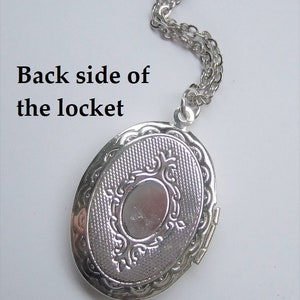May include: Silver oval locket with a decorative design on the back. The locket is attached to a silver chain.