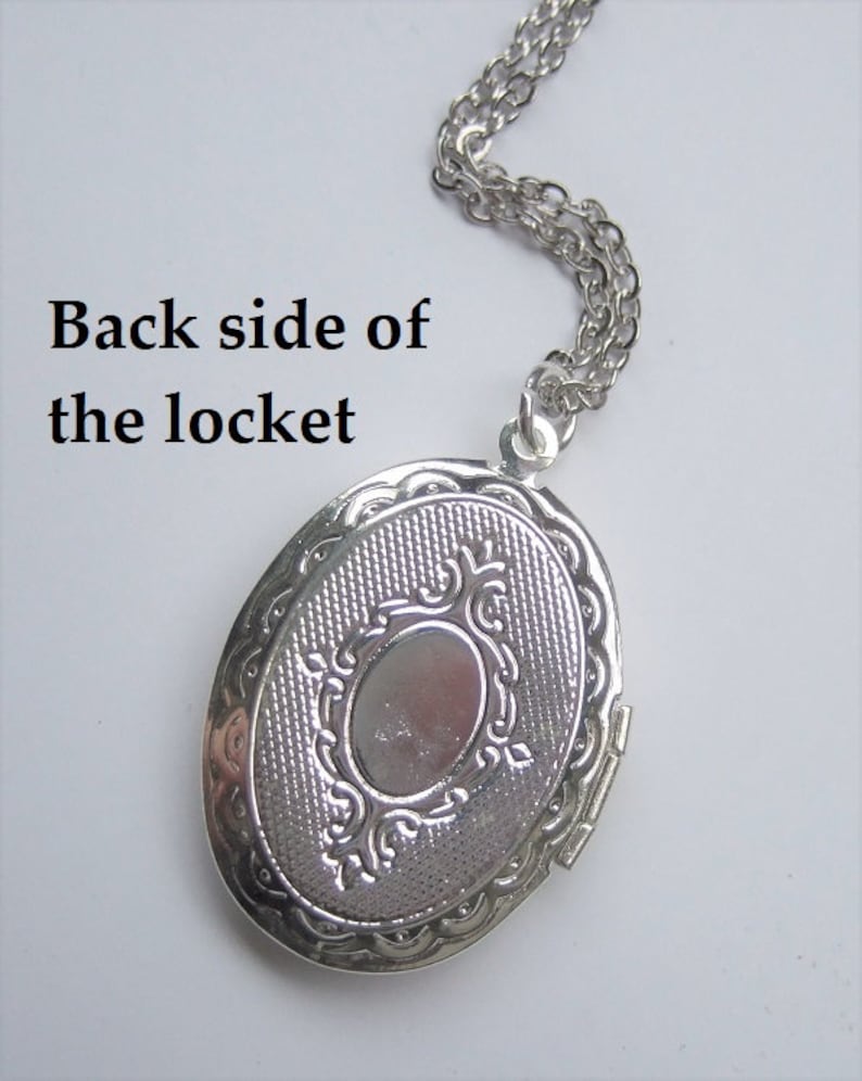 May include: Silver oval locket with a decorative design on the back. The locket is attached to a silver chain.