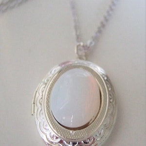 May include: A silver locket necklace with a white oval-shaped stone in the center. The locket has a detailed, ornate design around the edge.