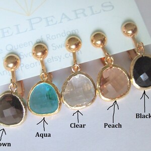 Puede incluir: Cinco pares de pendientes de clip dorados con gotas de piedras preciosas de diferentes colores. Los colores son marr&oacute;n, aguamarina, transparente, melocot&oacute;n y negro.