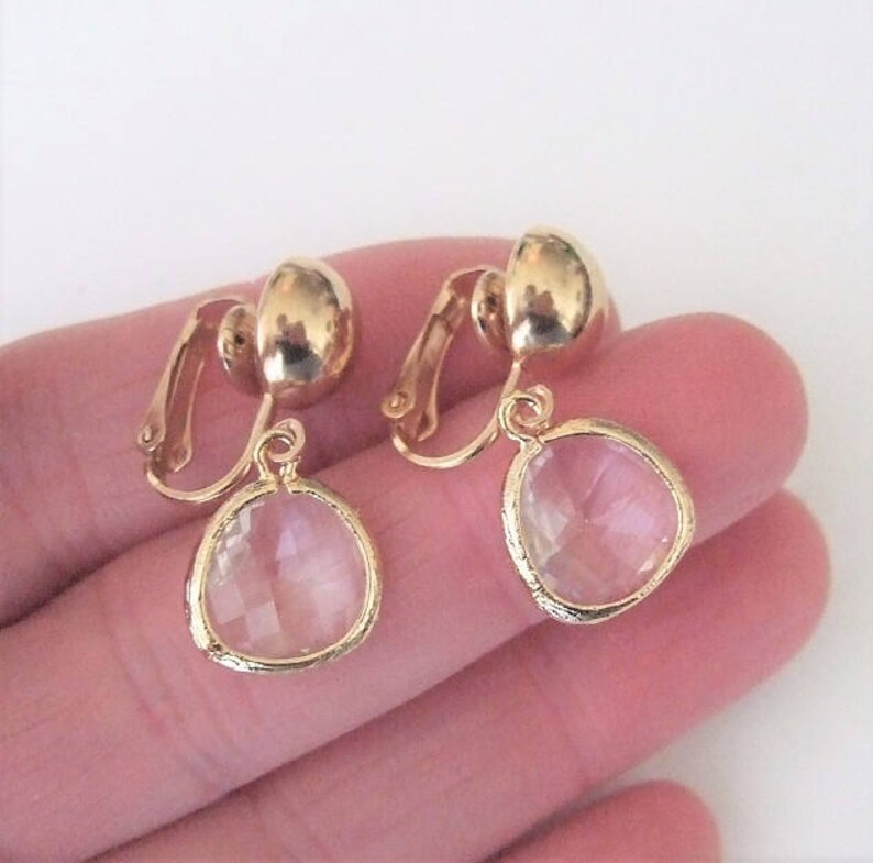 Puede incluir: Un par de pendientes de clip dorados con cristales transparentes en forma de l&aacute;grima.