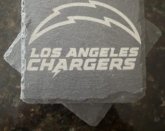 May include: A square dark gray slate coaster featuring the white engraved Los Angeles Chargers lightning bolt logo and the team name text. The coaster has a rough, natural stone texture with uneven edges, stacked atop another identical slate coaster.