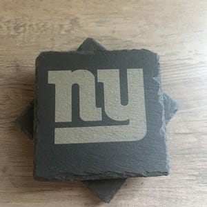 May include: Two black slate coasters with a silver 'NY' logo. The coasters are stacked on top of each other.