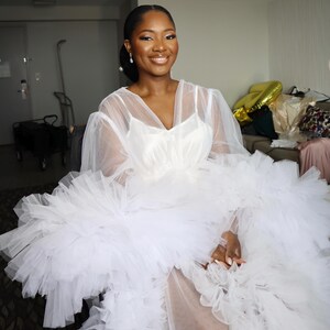 May include: A white tulle dress with a ruffled skirt and sheer long sleeves.