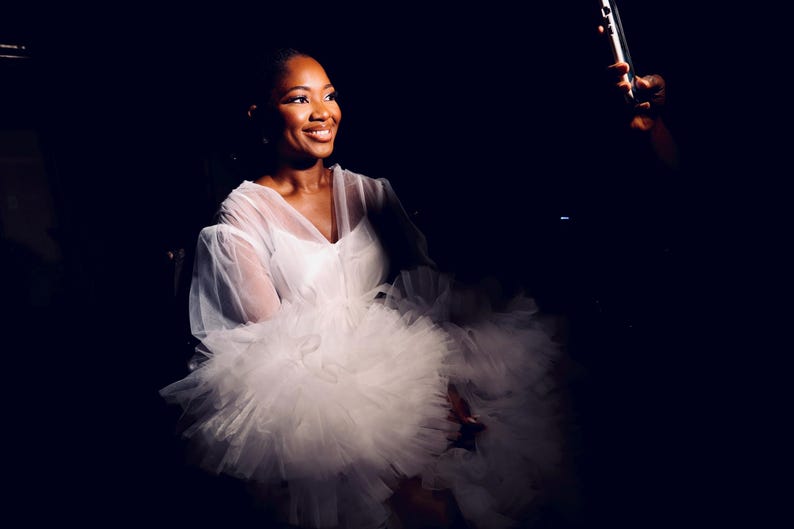 May include: A woman wearing a white tulle dress with a sheer overlay.