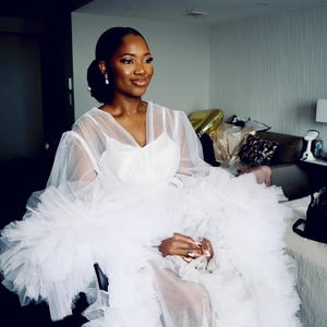 May include: A white tulle gown with ruffled sleeves and a plunging neckline.