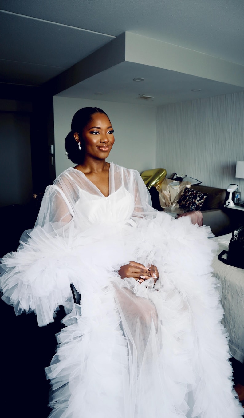 May include: A white tulle gown with ruffled sleeves and a plunging neckline.