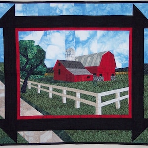 May include: A red barn with a white fence in front of it. The barn is surrounded by green grass and a blue sky with white clouds. The image is framed with a black border.