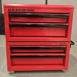 May include: A red U.S. General rolling tool chest with four drawers and black drawer pulls. The top of the chest has the words "U.S. GENERAL" in black. The bottom of the chest has the word "Milwaukee" in black.