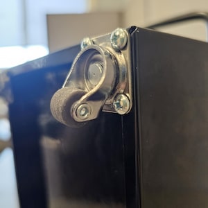 May include: Close-up of a black metal toolbox with a silver caster wheel. The wheel has a black rubber tire and a silver metal frame.