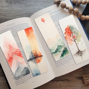 May include: Set of four watercolor bookmarks featuring nature scenes. The bookmarks include a mountain range, a lake with trees reflected in the water, a mountain range with a sunset, and a tree with red leaves.