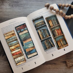 May include: An open book with four decorative bookmarks featuring stacks of vintage books and bookshelves. The bookmarks are rectangular with a distressed, aged appearance. A wooden bead garland and a black tray with greenery are also present.